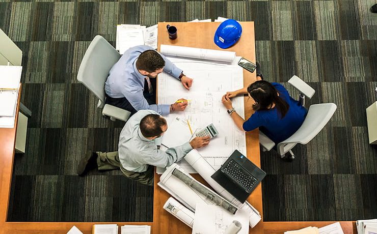 Picture of architects at work studying plans. The workflow in architecture firms can be improved significantly by the use of project management software specifically for architecture.